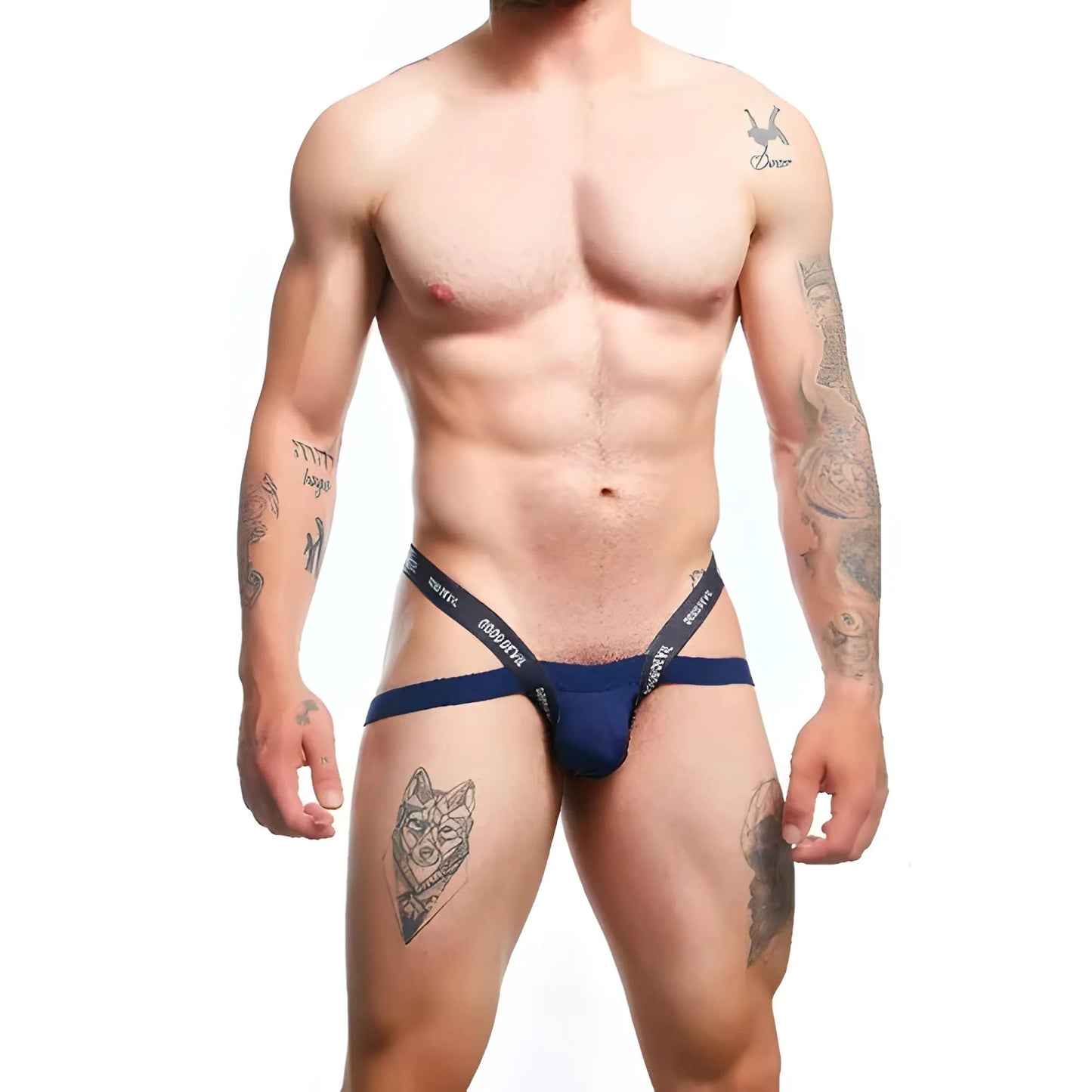 A muscular individual stands confidently against a white backdrop, clad in a blue Good Devil Sexy Men Jockstrap. Tattoos on their arms and one leg accentuate the look, perfectly complemented by the jockstraps Premium Fabric Blend.