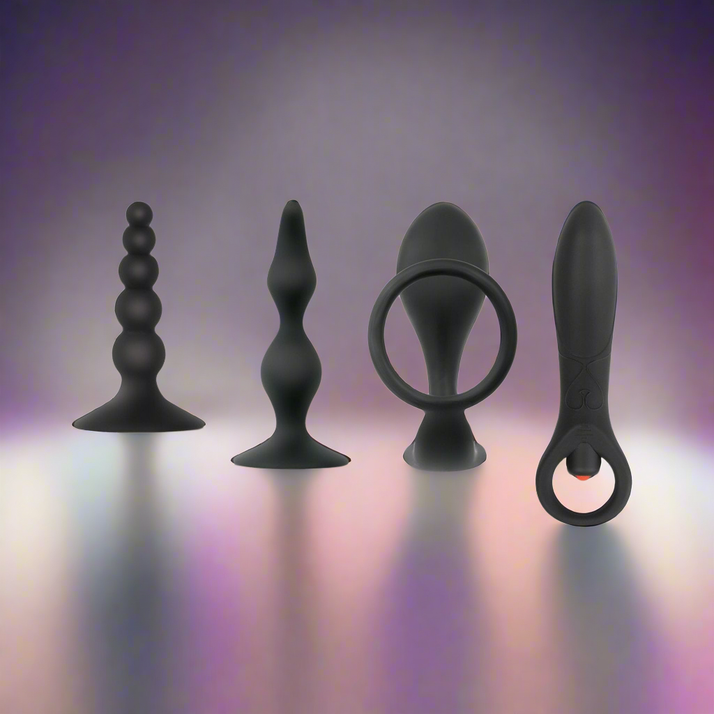 Against a purple gradient, the Zero Tolerance Intro To Prostate Kit by Zero Tolerance showcases four black body-safe silicone toys. Each toy, in unique shapes like beads, spirals, and loops, stands upright with light gently reflecting off their surfaces.