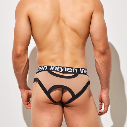 A person is standing against a white background, wearing Intymen Desert Jockstrap Crotchless Underwear in beige and black. The design features a supportive fit, an open back, and has Intymen on the waistband.