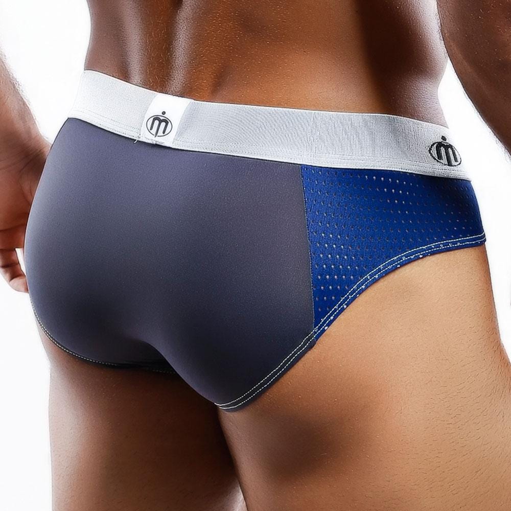 Someone is dressed in a snug blue and gray Intymen Vibrant Attitude Bikini Brief with a white logo waistband, highlighted by its modern sporty style, contoured center pouch, and textured side pattern. The softly blurred background enhances the look.