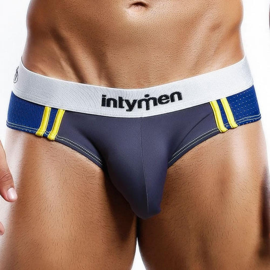 A person wears Intymen Vibrant Attitude Bikini Briefs in blue and gray, featuring a white waistband with the brand name, yellow side stripes, and a contoured pouch for support, highlighting its stylish design.