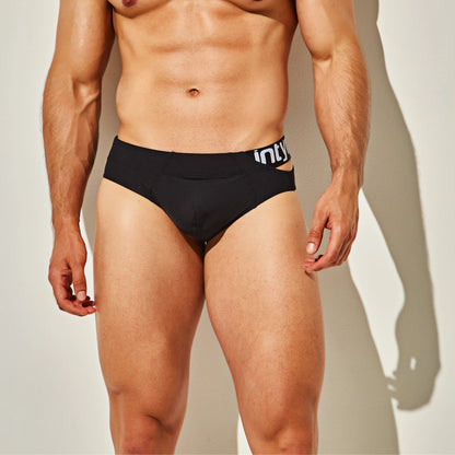 A person stands against a plain wall, wearing black Intymen True Brief Underwear. The waistband features a partially visible logo, with a slim fit and premium fabric blend that offers style and comfort.