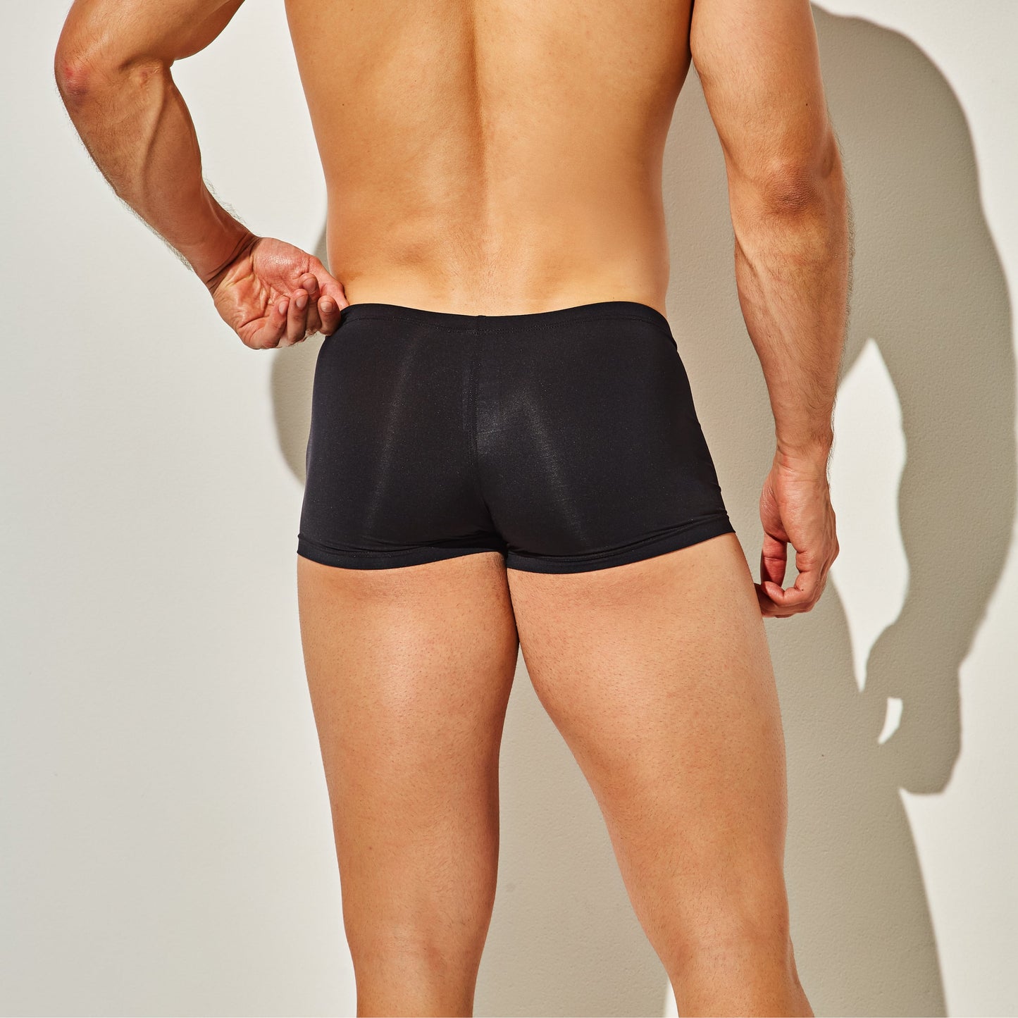 A person stands against a plain background wearing Intymen Star Pouch Boxer Trunk Underwear, showcasing their back and legs. A slight shadow accentuates the soft, stretchy fabric and spacious pouch designed by Intymen for ultimate comfort.