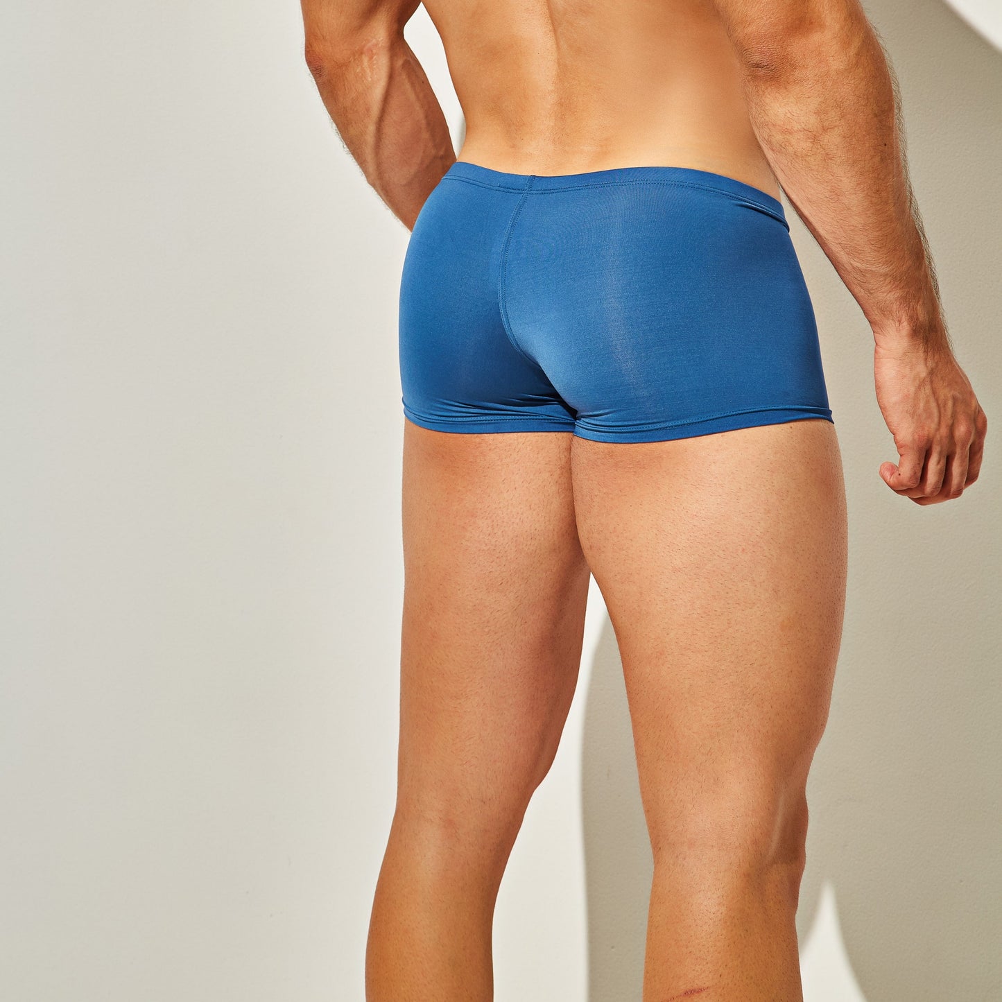 A fit individual wears Intymen Star Pouch Boxer Trunk Underwear in tight blue, standing against a softly lit neutral background. The focus is on the soft, stretchy fabric and spacious pouch engineered for maximum comfort.