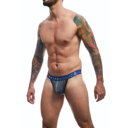 A tattooed man stands against a white background wearing the Malebasics Male Basics Hipster Jockstrap Andalusia, which showcases a blue and white pattern with a low-cut elastic waistline.
