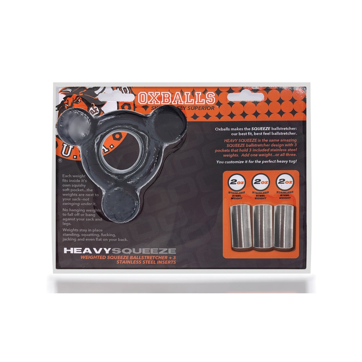 The Oxballs Heavy Squeeze Ballstretcher comes in transparent packaging that displays its balanced design and stainless steel weights labeled 2 oz. The package features striking orange and black accents with brand and product details.