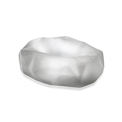 A translucent, irregularly shaped object with a matte finish, resembling a small shallow dish, subtly echoes the design of the Hunky Junk Fractal Cockring by Hunky Junk. Set against a plain white background, it invites curiosity and exploration.