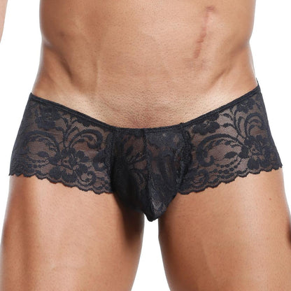 Someone wearing the Secret Male Slip Bikini, showcasing its black lace with a floral pattern against a plain background. The upper body is partly visible, emphasizing the underwears flexible fit and design.