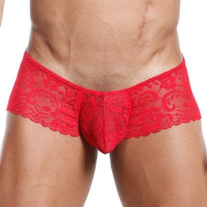 A person models Secret Males Slip Bikini, showcasing a red lace design with an intricate floral pattern and contoured pouch, ensuring a flexible fit. The image highlights the wearers toned abdomen and legs.