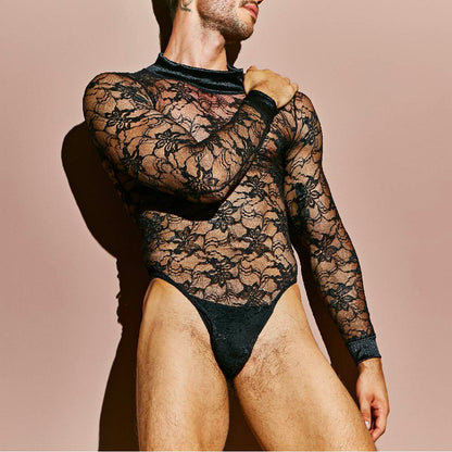 Someone is wearing the Secret Male Mens Lingerie Sexy Bodysuit, featuring alluring black lace with a floral pattern. Against a plain beige background, the long-sleeved suit hugs the body and is slightly sheer. The persons head is turned to the side and not visible.