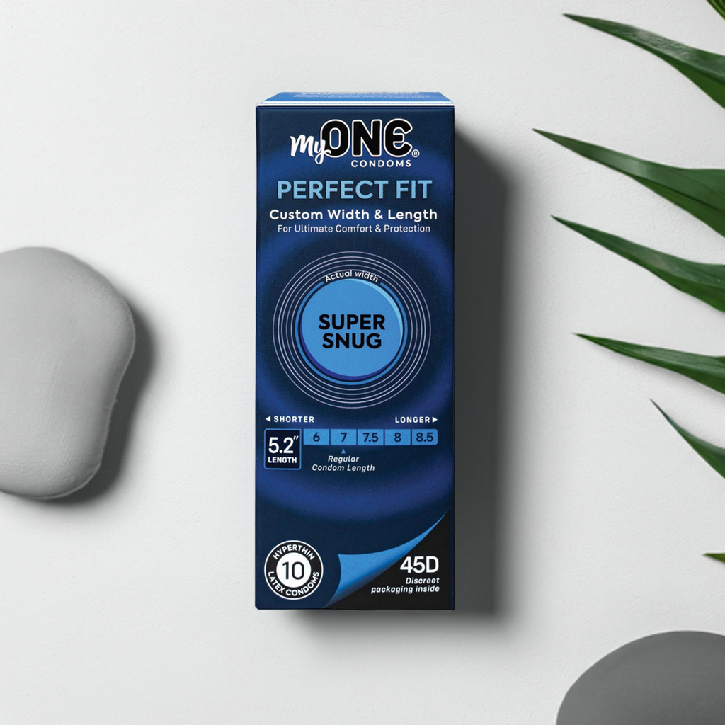 A blue box of Paradise Marketings My One Super Snug Condoms labeled Perfect Fit is on a white surface with a plant and gray stones. The box features 45 custom-sized condoms and notes a 5.2-inch length for personalized comfort.