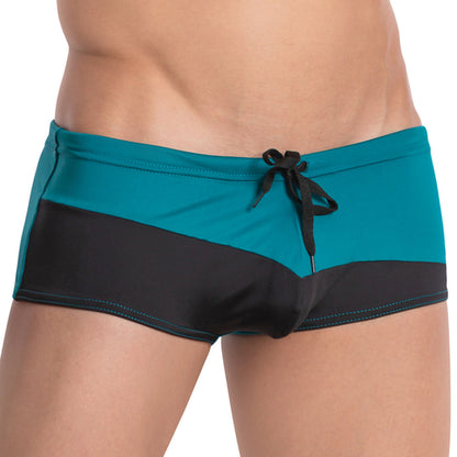 Close-up of someone wearing Agacio Ocean Swim Trunk by Agacio, featuring a teal and black color-block design with an adjustable drawstring, showcasing a teal top and bold black diagonal band.