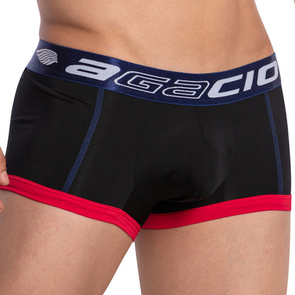A person wears Agacio Stretch Boxer Trunks in black and red, featuring a blue waistband with white branding. The trunks offer comfort with a double-stitched pouch and stylish blue stitching accents while slightly adjusting the left side of the waistband.
