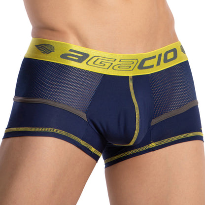 A person wearing the Agacio Multi Color Piping Boxer Trunk in navy blue and yellow with colorful piping on the mesh sides. The yellow waistband features the brand name, designed from a premium fabric blend for maximum comfort.