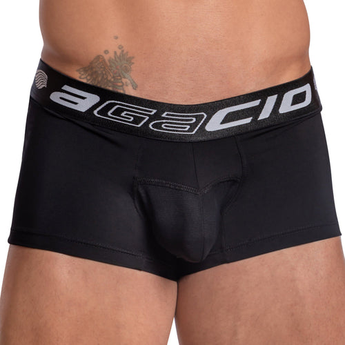 A person wearing Agacio Contour Pouch Boxer Trunks with a visible logo on the waistband is seen. A tattoo peeks above the left waistband. The photo emphasizes their waist and upper thighs against a plain backdrop.