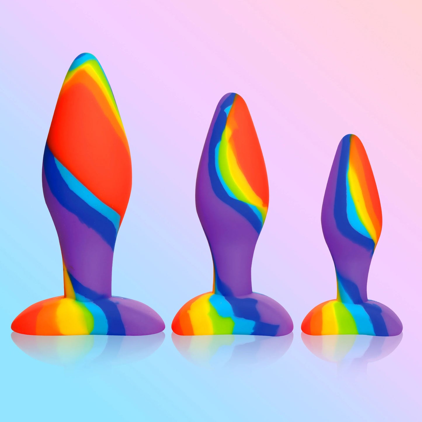 The Curve Novelties Simply Sweet Rainbow Silicone Butt Plug Set, featuring three body-safe silicone plugs with wider bases, is arranged against a pastel gradient background.