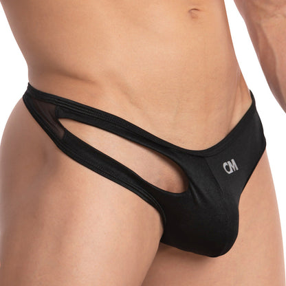 A close-up of a person wearing the Cover Male Left Side Thong highlights its sexy sheer design and unique side cutouts. The body-hugging fit accentuates every curve, featuring CM on the front, emphasizing its innovative design and material.