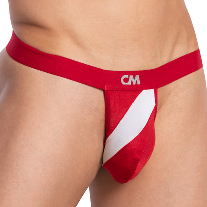 A person models the Cover Male Bi-Color Sexy Thong in a red and white design featuring CM on the waistband, a supportive pouch, and a prominent diagonal white stripe highlighting the midsection and upper thigh.
