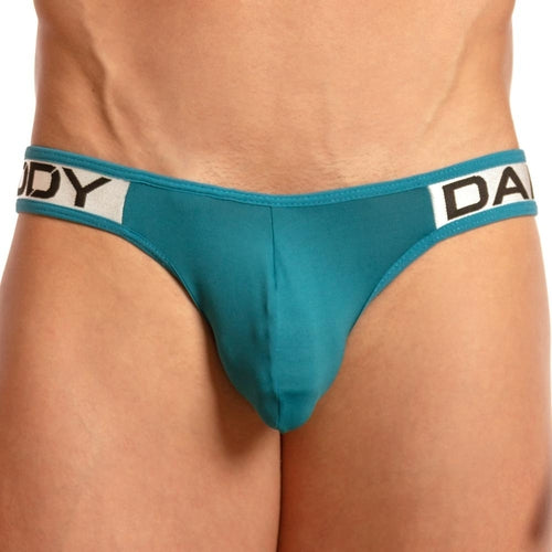 The model wears a Daddy Invisible Jockstrap, turquoise with a black and white DADDY waistband, featuring an enticing pouch design against a neutral backdrop, emphasizing its barely-there style.