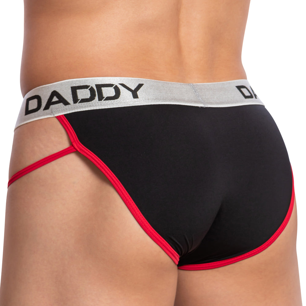 A person wearing a Daddy Alluring Brief, featuring an enhancing pouch with black material, red trim, and a gray waistband displaying DADDY in bold black letters. The side angle highlights the sleek design on the lower back and underwear.