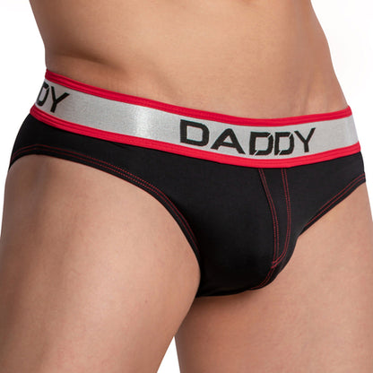 Close-up of someone wearing the Daddy Dazzler Brief with black briefs, red stitching, and a silver waistband. The shiny stretchy fabric enhances the body while DADDY on the waistband draws attention to the lower torso and underwear.