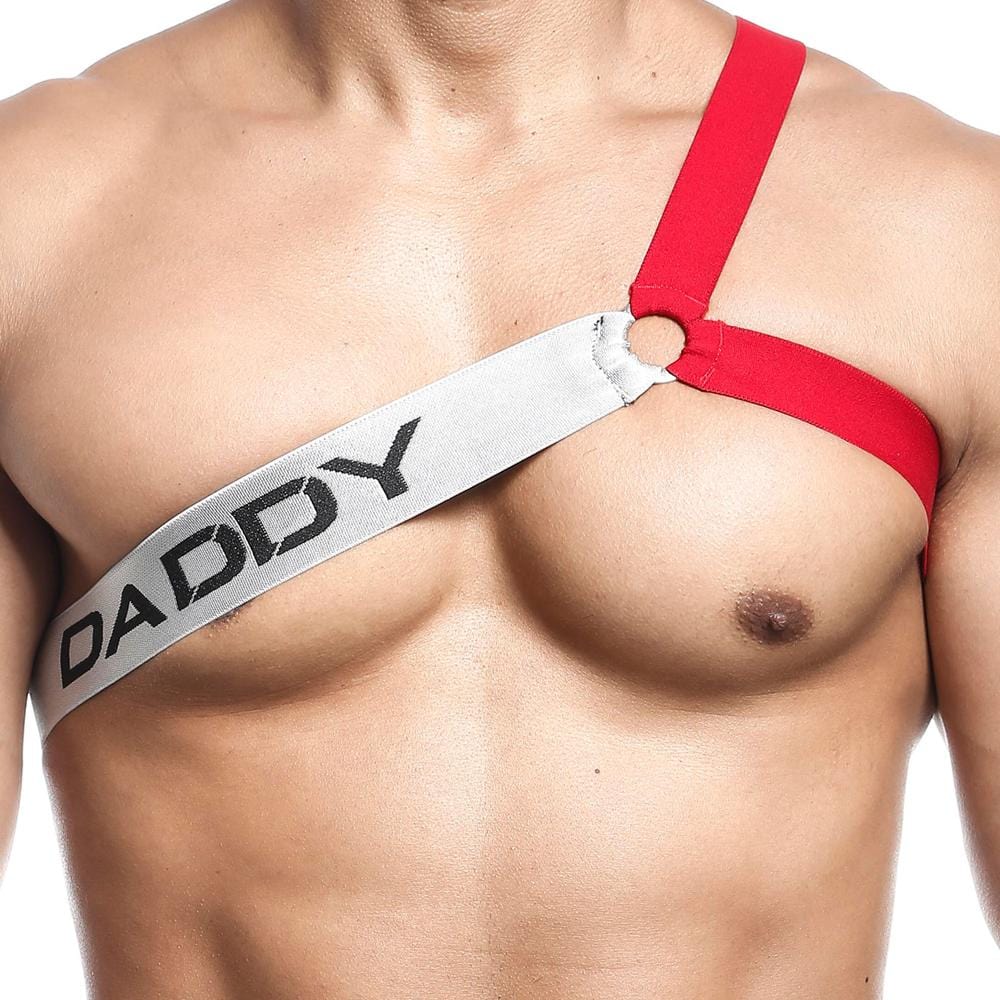 The Daddy Harney Man Strap by Daddy showcases a close-up of a person wearing its sexy one-shoulder harness with red and white straps. Featuring a unique three-strap design, it displays DADDY in bold black letters diagonally across the chest for an edgy look.