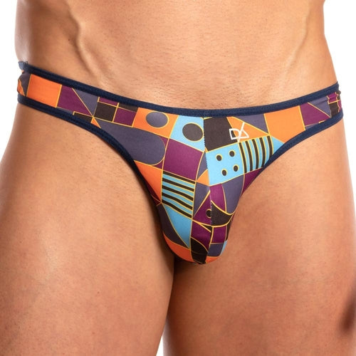A person is wearing the Daniel Alexander Limited Ass Kini Thong, featuring colorful geometric patterns with a dark blue outline and a sleek, stretchy waistband. The design includes shapes in shades of orange, purple, blue, and black, focusing on the persons lower torso.