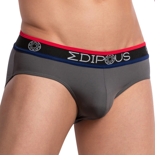 A person is wearing Edipous Munich Briefs, which are gray with a black waistband and red stripe, blue accent, and EDIPOUS in white. These mens bikini briefs offer luxurious comfort with decorative emblems on each side of the low-rise design.