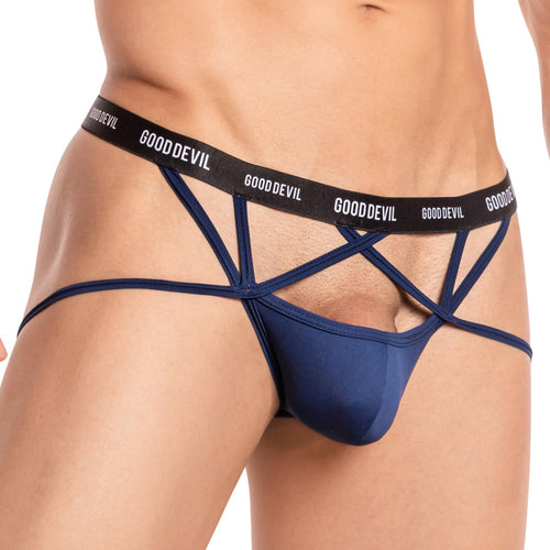 A person wears the Good Devil Ball Sling Jock, a navy blue jockstrap with a black GOOD DEVIL waistband. This minimal coverage piece has open sides and a supportive front pouch, featuring its unique ball sling design.