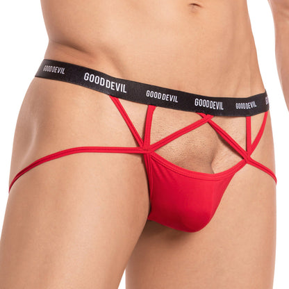 A person models the Good Devil Ball Sling Jock, featuring red strappy underwear with a black Good Devil waistband. Its minimal coverage includes open sides and intricate straps, emphasizing the ball sling design.