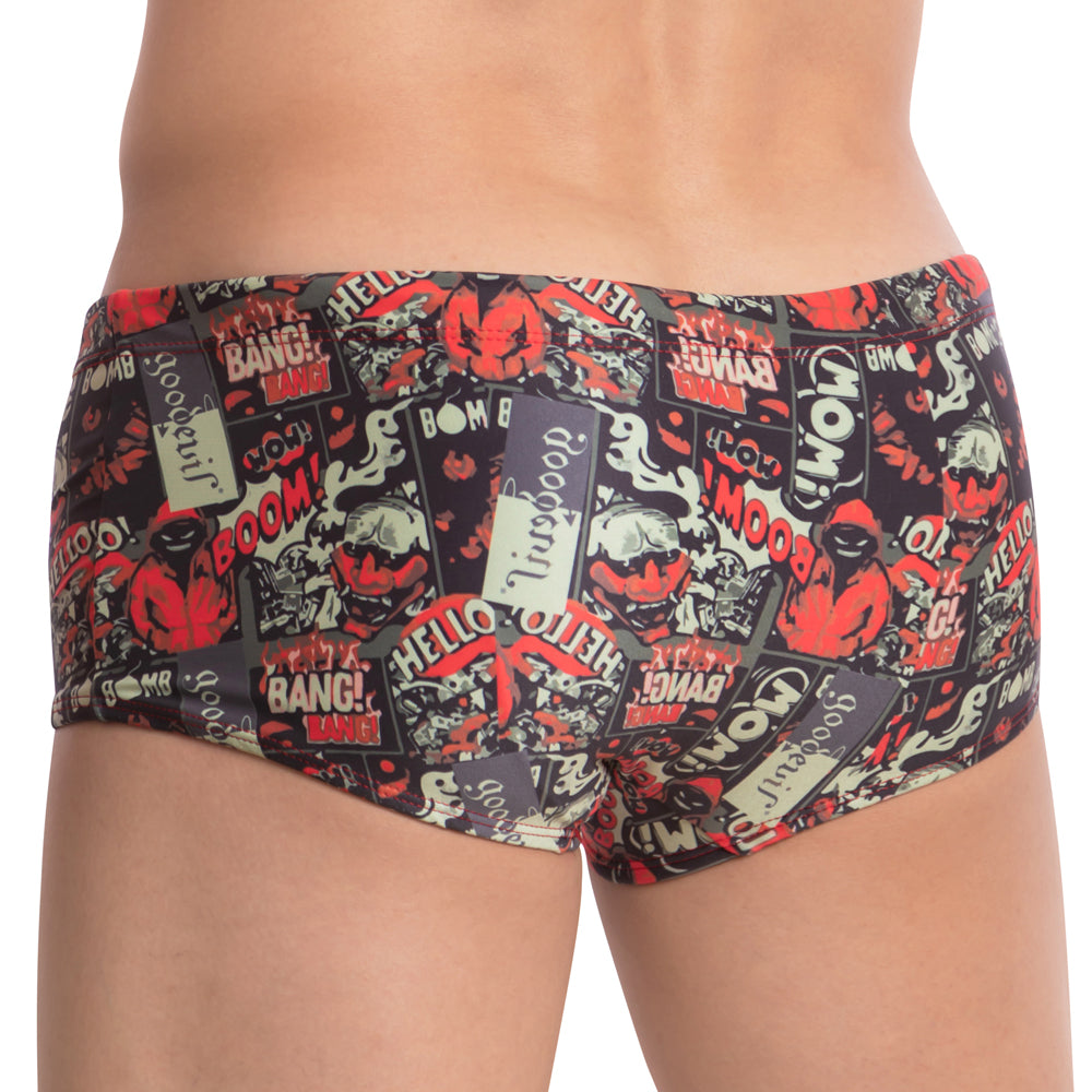 Wearing the Good Devil Playtime Boxer Trunk, a person displays vibrant swimwear featuring a nostalgic comic-style design with bold words like BOOM! and BANG! in red, black, and beige tones. They stand back to the camera, blending retro flair with modern fun.
