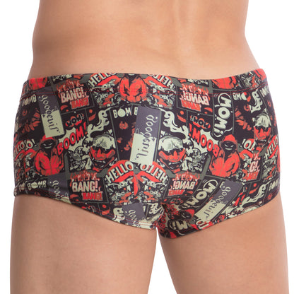 Wearing the Good Devil Playtime Boxer Trunk, a person displays vibrant swimwear featuring a nostalgic comic-style design with bold words like BOOM! and BANG! in red, black, and beige tones. They stand back to the camera, blending retro flair with modern fun.