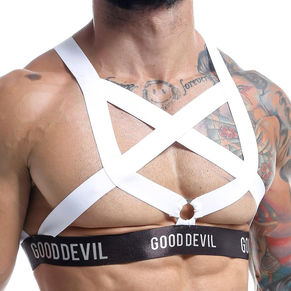 A person flaunts their chest with a white strappy Good Devil harness, GOOD DEVIL in bold on a black band. Tattoos accentuate the style against a pristine white background.