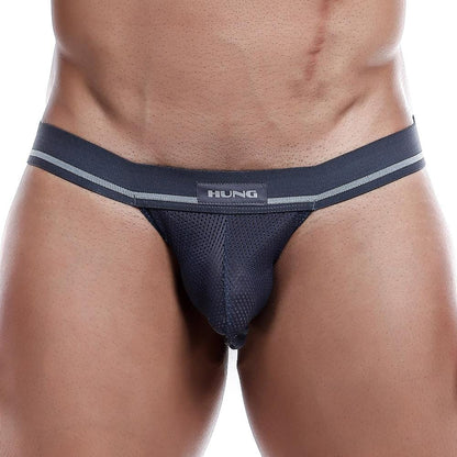 A model wears the Hung Jockstrap with a breathable mesh pouch and supportive straps, featuring a branded waistband. The focus is on the midsection to highlight the design and fit, while a plain background accentuates the garments sleek look.