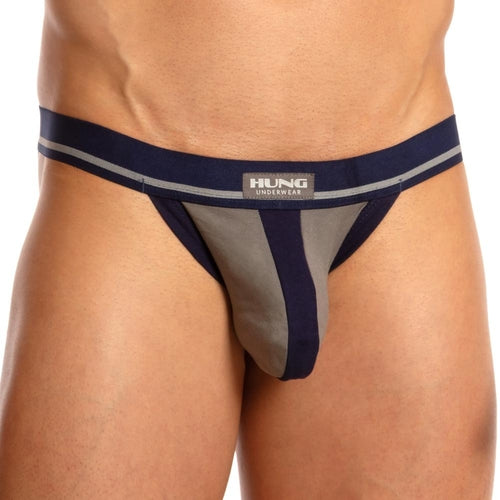 A person wears the snug-fitting Hung Dong Jock in grey and navy, showcasing a bold design with a branded Hung waistband. The focus is on the lower torso, with supportive elastic straps ensuring comfort.