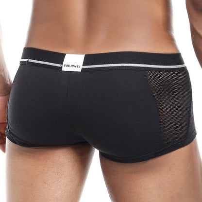 A person wears the Hung Clash Trunk, featuring black fitted underwear with a mesh side panel. The rear waistband displays the Hung brand name, highlighting a sleek Fabric Fusion design. The focus is on the Contour Pouch and lower back for optimal fit, comfort, and style.