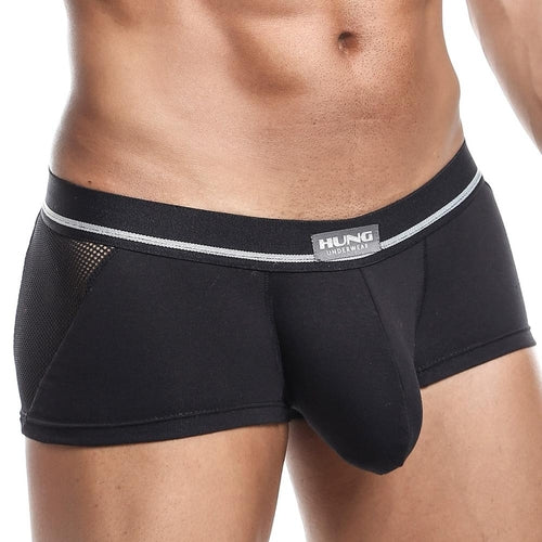 A model wears black Hung Clash Trunk boxer briefs by Hung, showcasing a wide elastic waistband with HUNG Underwear branding, side mesh panels, and a contour pouch. The torso is visible but the face remains hidden.
