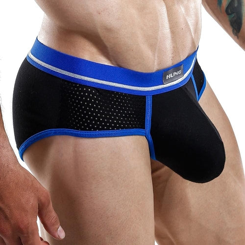 Close-up of a person wearing black and blue Hung Brief by Hung, showcasing breathable mesh panels and a branded waistband. The focus is on the design, functional pouch, and athletic fit of these underwear.