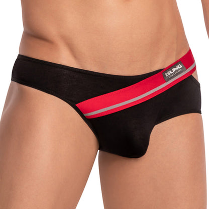 A person is modeling the Hung Ivan Brief, featuring black mens bikini briefs with a red and silver waistband. The visible Hung label highlights a snug fit and enhancing pouch, set against a plain backdrop for style and comfort.