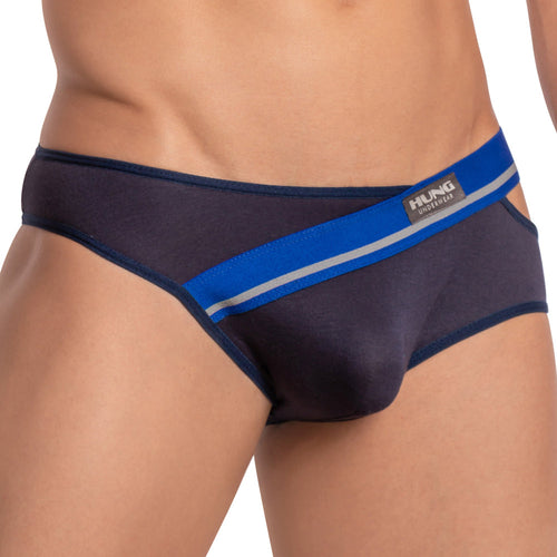 A person in Hung Ivan Briefs, navy blue mens bikini style, with a striped blue and white waistband, branded label on the front, and a butt-enhancing design for added lift.