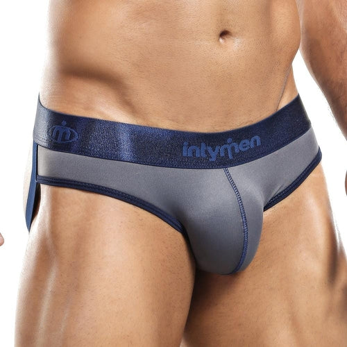 A muscular individual in Intymen Jockstrap briefs, featuring a dark blue and gray design with a shiny branded waistband. The classic style showcases elegant stitching, accentuating the sleek jockstrap lines. The persons midsection and part of their thighs are visible.