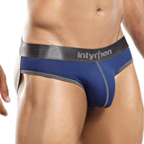The image shows a person wearing blue and black Intymen Jockstrap underwear, highlighting elegant stitching. The classic design features a wide black waistband with silver logo lettering and gray edge trim, captured from mid-chest to mid-thigh.