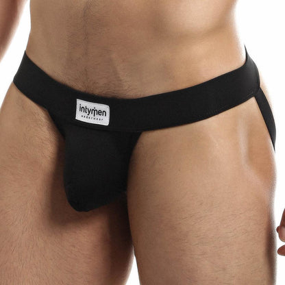 A person is shown from the waist to upper thighs wearing a black Intymen Proud Jock, displaying a supportive fit with its wide waistband and contoured pouch, against a plain white background.