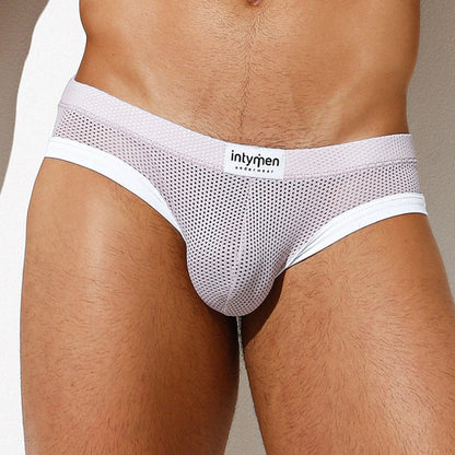 A person wearing Intymen Dolce Jockstrap enjoys a comfortable fit, featuring white mesh with a small logo patch on the waistband. The image focuses on the lower torso and thighs against a neutral background, highlighting the supportive pouch for added comfort.