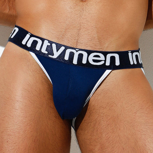 A person wearing the Intymen Trevi Jockstrap in blue with a black waistband featuring intymen in white. The sleek design includes white side straps and a supportive contoured pouch, set against a neutral background.