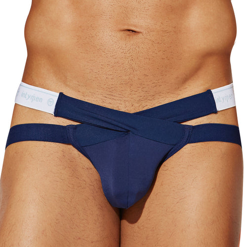 A person wears a navy blue Intymen Cross Strapped Jockstrap, showcasing a seductive white waistband with branding. It features a distinctive front design with extra blue straps, made from stretchy fabric, against a plain white background.