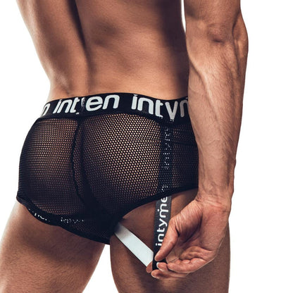 The image depicts a person from the back wearing Intymen Jock Mesh Cover, featuring black mesh underwear with a white strap and branded waistband. The design details and supportive fit are accentuated on a plain background, showcasing the breathable mesh fabric.