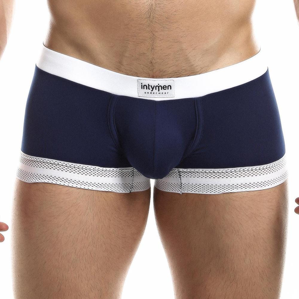 A man confidently wears the Intymen Quads Trunk with a tailored fit in navy blue, a white waistband, and sleek mesh trim, showcasing premium quality and featuring the Intymen brand label for a signature finish.