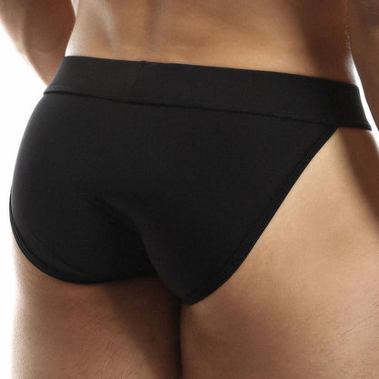 The image displays a rear view of someone wearing Intymen Obscene Bikini in black, showcasing its high-cut design. The focus on the lower back and hips emphasizes the sleek, smooth material and comfortable fit.