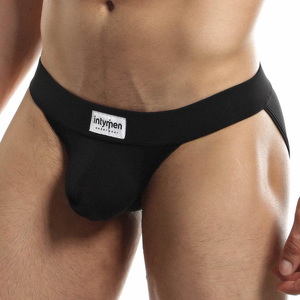 A person wearing a black Intymen Obscene Bikini with a high-cut design, emphasizing the waistband and pouch area for comfort. The background is plain white.